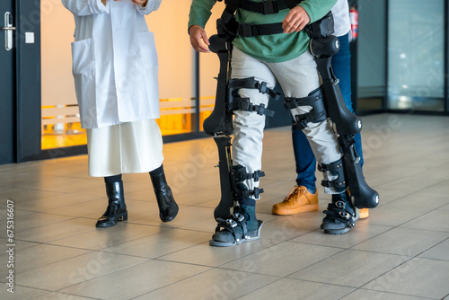 Mechanical exoskeleton, female doctor with unrecognizable engineer walking with disabled person with robotic skeleton in rehabilitation, physiotherapy in a modern hospital, futuristic physiotherapy