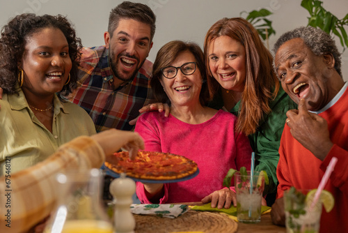 Group of multiracial friends, of different ages, generations, celebrating a pizza dinner in a restaurant, selfie with smart phone