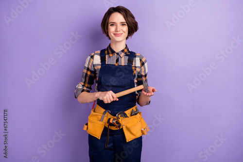 Photo of young woman builder craftsman hold hammer tools repair restoration isolated over violet color background