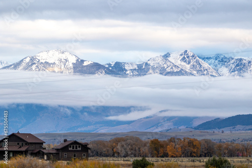 Log cabins with a forest view and low level cloud, snow covered mountains on the outskirts of Yellowstone national park on a cold autumn's day