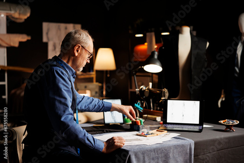 Elderly fashion designer preparing his atelier shop workspace before starting work on upcoming sartorial collection. Couturer picking necessary sewing materials for client comissioned attire