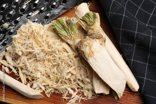Grated horseradish, peeled roots and grater on wooden board, closeup