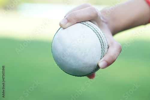 Close up bowler hand holds a white leather cricket ball. Concept, sport equipment. Competitive sport. A cricket ball is made with a core of cork, covered by a leather case. Ready to bowl to batsman