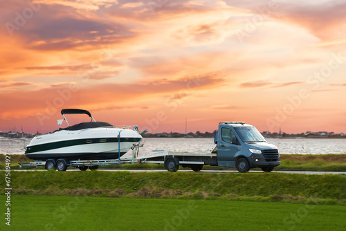 Luxury Boat Journey on the Road at Sunset. Modern motorboat delivery on the driveway. Sunset sky.