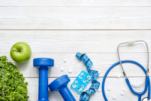 Composition with dumbbells, measuring tape, pills and healthy food on white wooden background