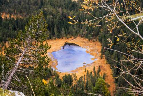 Pequeño lago, visto desde lo alto de la montaña, con forma de una especie de cara, rodeado de árboles verdes y vegetación amarilla.