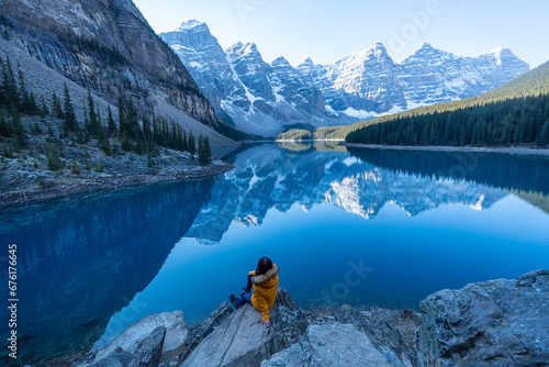 Female tourist carries a backpack, travels, walks, climbs, sits and admires the beauty of the reflection in the water of moraine Lake, Canadian Rocky Mountains