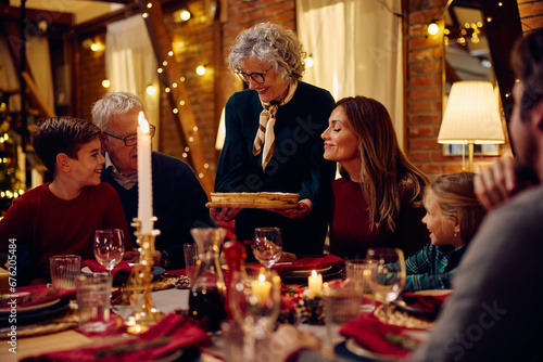 Happy senior woman serving Christmas pie to her family at dining table.