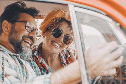 Happy couple having fun inside a car during travel adventure. Cheerful man and woman smiling and laughing a lot together. People enjoying vehicle trip in friendship and relationship. Concept of drive