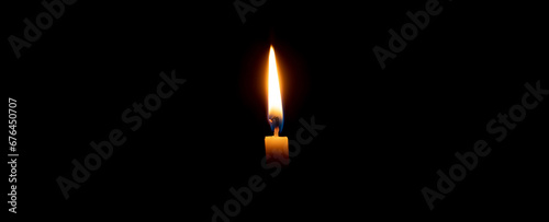 A single burning candle flame or light glowing on an orange candle on black or dark background on table in church for Christmas, funeral or memorial service with copy space
