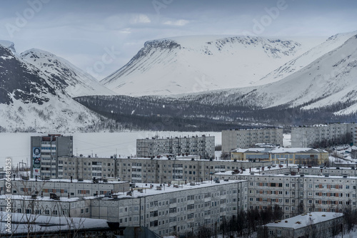 The aerial photo of Kirovsk city in Murmansk oblast of Russia, with the Soviet-style apartment buildings, the snow-covered Khibiny mountains during the winter day.