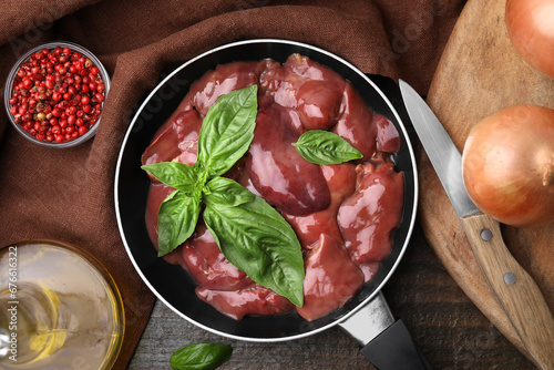 Raw chicken liver with basil in frying pan and products on wooden table, flat lay