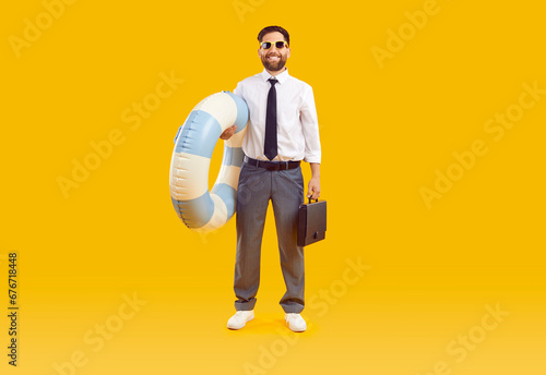 Happy businessman combines business trip and summer holiday. Full body length adult man in office wear with water floatie and briefcase standing isolated on yellow background. Vacation, travel concept