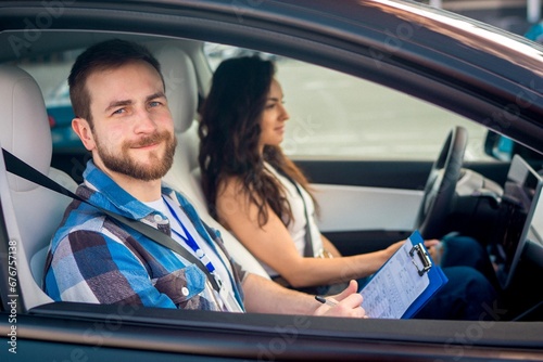Young woman driving a car with male instructor. Lady looking on the road, man holding test drive report. Test drive, transportation, safety, education concept