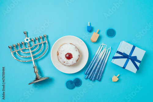 Jewish holiday Hanukkah top view composition with menorah, traditional donuts and gift box on blue background. Flat lay