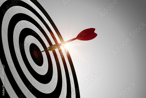 Red dart with reflected light hitting the center of the dartboard, concept of reaching the specified target and winning goals business concepts.