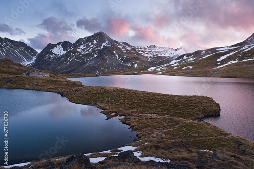 Golden Hour Bliss: Cabin by the Lake with a Majestic Sunset, Snow-Capped Mountains in the Background