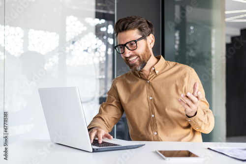 Online video call, remote conversation, man smiling at presentation talking to colleagues and partners, businessman working inside office with laptop, wearing shirt and glasses