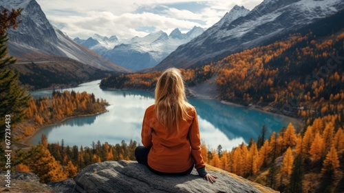 Traveler millennial girl in yellow beanie hat with backpack sitting on cliff edge with autumn forest and enjoying beautiful valley view. Adventure vacations