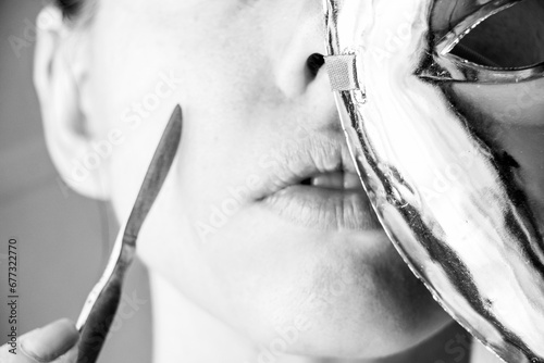 A surgical scalpel is in the hands of a girl next to her face, and a plastic mask covers her face, beauty and fashion