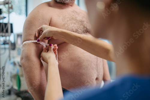 Female doctor measuring arm circumference of overweight patient using tape measure. Obesity affecting middle-aged men's health. Concept of health risks of overwight and obesity.