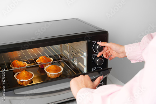 Woman's hands taking buscuit cupcakes out of mini oven