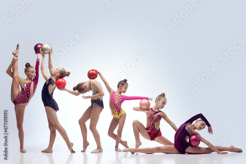 Group of beautiful little girls, children, rhythmic gymnasts in stage clothes dancing with balls against white studio background. Concept of choreography, hobby, art, sport, childhood, performance