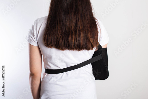 A girl on a white background with a black supporting medical bandage after a dislocation of the shoulder joint and a bone fracture. Rehabilitation after injury, orthopedics and traumatology