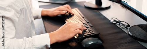 Office worker sitting on workspace desk, focused and engaged, using computer and typing on keyboard to input data ensure accurate data management in the modern workplace. Trailblazing