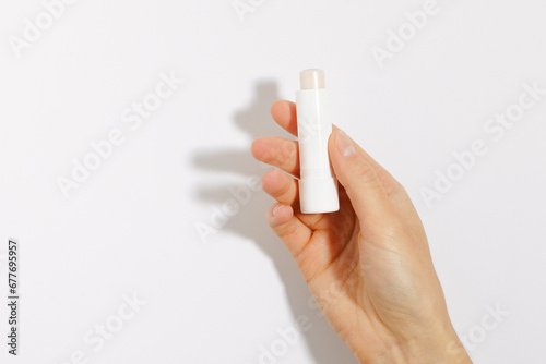 Female hand holding clear protective lip balm on white isolated background. Mockup for your design. The concept of decorative cosmetics for health and beauty