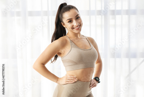 Portrait of sporty positive young woman in sportswear against window