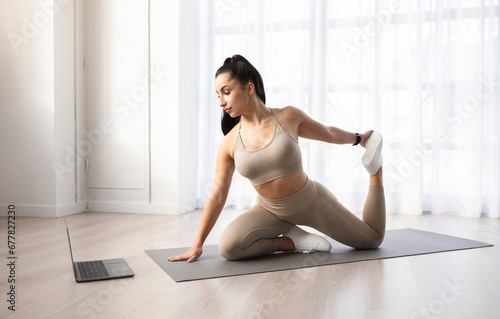 Athletic young woman doing yoga at home, watching fitness video