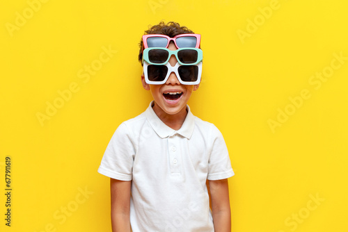 shocked african american boy with three sunglasses showing surprise on yellow isolated background