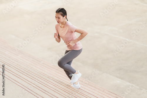 Full length sporty young Asian woman running on steps. Young female in sportswear jogging while exercising on the steps outdoor.