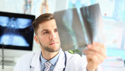 Portrait of thoughtful doc examining x-ray picture. Concentrated physician making diagnosis. Medical treatment and health care concept. Blurred background