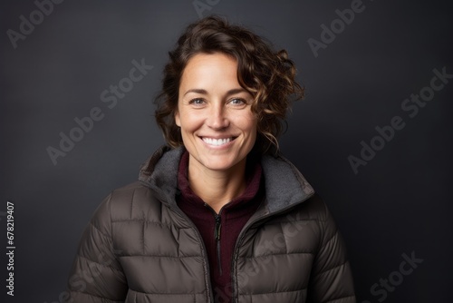 Portrait of a smiling woman in her 40s sporting a quilted insulated jacket against a plain cyclorama studio wall. AI Generation