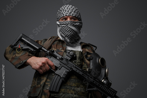 Middle Eastern radical fanatic soldier donning a white keffiyeh and camouflaged field uniform, armed with an automatic rifle, against a gray background