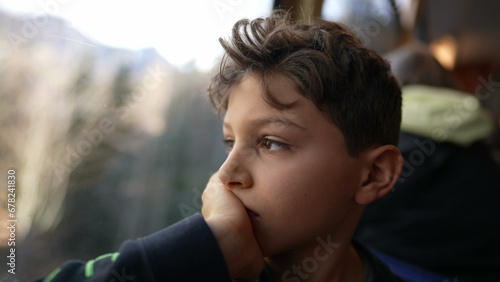 Melancholic young boy sitting by train window looking at view with hand in chin, thoughtful pensive expression of pre-teen child traveling and daydreaming
