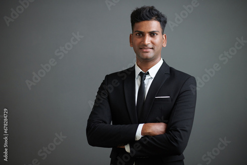 Studio portrait of smiling confident young businessman in suit crossing arms and looking at camera