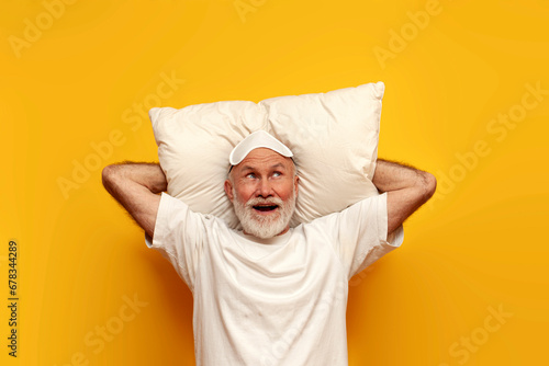 old bald grandfather in pajamas and sleep mask lies on pillow and imagines on yellow isolated background