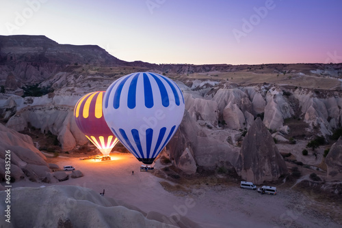 two hot air balloons full of tourists, about to take off at dawn between fairy chimneys, service vans around the balloons, cappadocia turkey