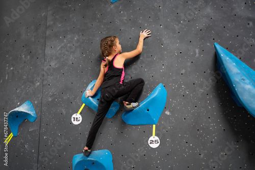 Little girl in sports clothes climbing wall of an entertainment centre. Child climbing wall at professional rock climb centre without use of hands. Child enjoys his hobby. Climb centre