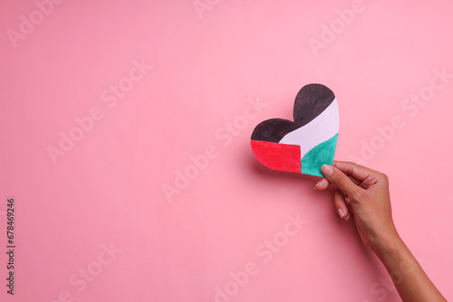 Hand holding a heart shaped paper with the colors of the Palestinian flag on a pink background