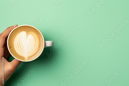 Top view of a hand holding a hot cup of coffee on a pastel green background with space for text. 