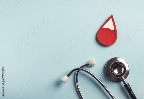 Red blood drop with medical stethoscope on pastel blue background. Iron deficiency anemia, hemophilia, blood donation concept. Top view, copy space
