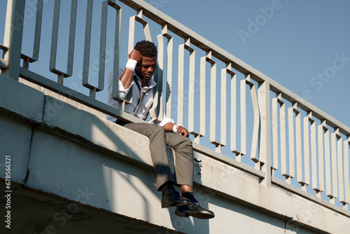 African American depressed man with bandaged wrists sitting on the bridge and thinking about suicide