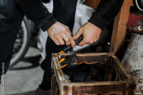 An adult male professional woodworker carpenter glues a chair, repairs, restores furniture in the workshop, clamping wooden products with a clamp. Photography, work concept, portrait.