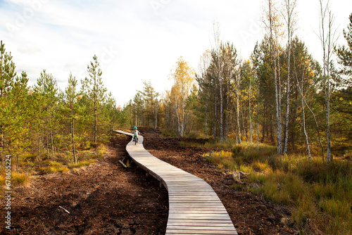 Small child riding on a bike on a wooden path through wetlands in National Park Sumava in autum