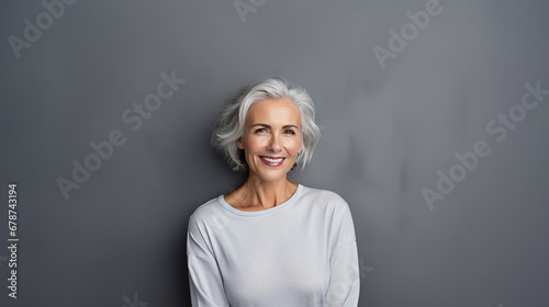 Close up portrait of beautiful older woman smiling and standing by grey wall.