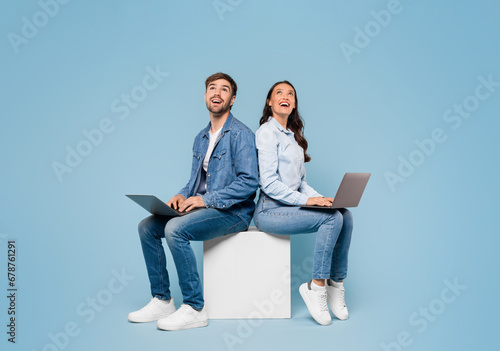 Couple with laptops look at free space on blue background